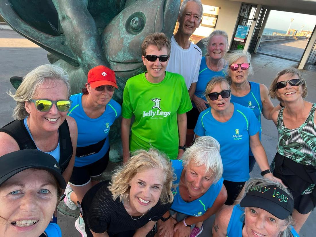 A smiling group of Jelly Legs members by the fish sculpture at Deal Pier on an evening run