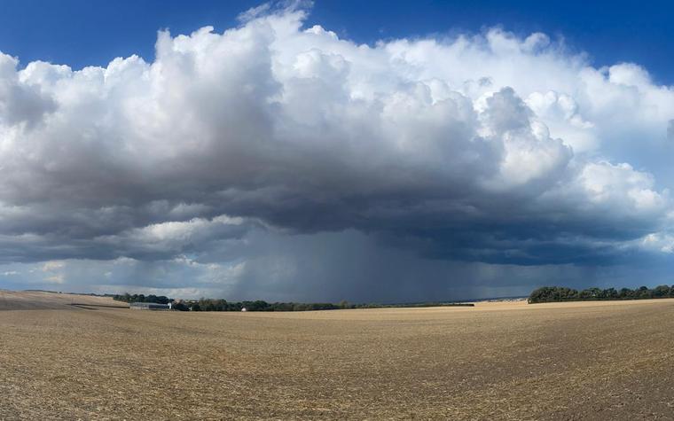 A dark rain cloud passing over open fields in the Kent countryside